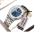 Une montre-bracelet pour homme en acier inoxydable de couleur argentée, avec un cadran bleu, un affichage de la date et une étiquette de prix de vente attachée.