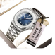 Une montre-bracelet pour homme en acier inoxydable de couleur argentée, avec un cadran bleu, un affichage de la date et une étiquette de prix de vente attachée.